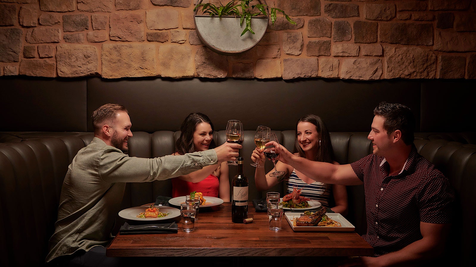 Four friends cheers their wine glasses at a booth in Mason Bar and Kitchen